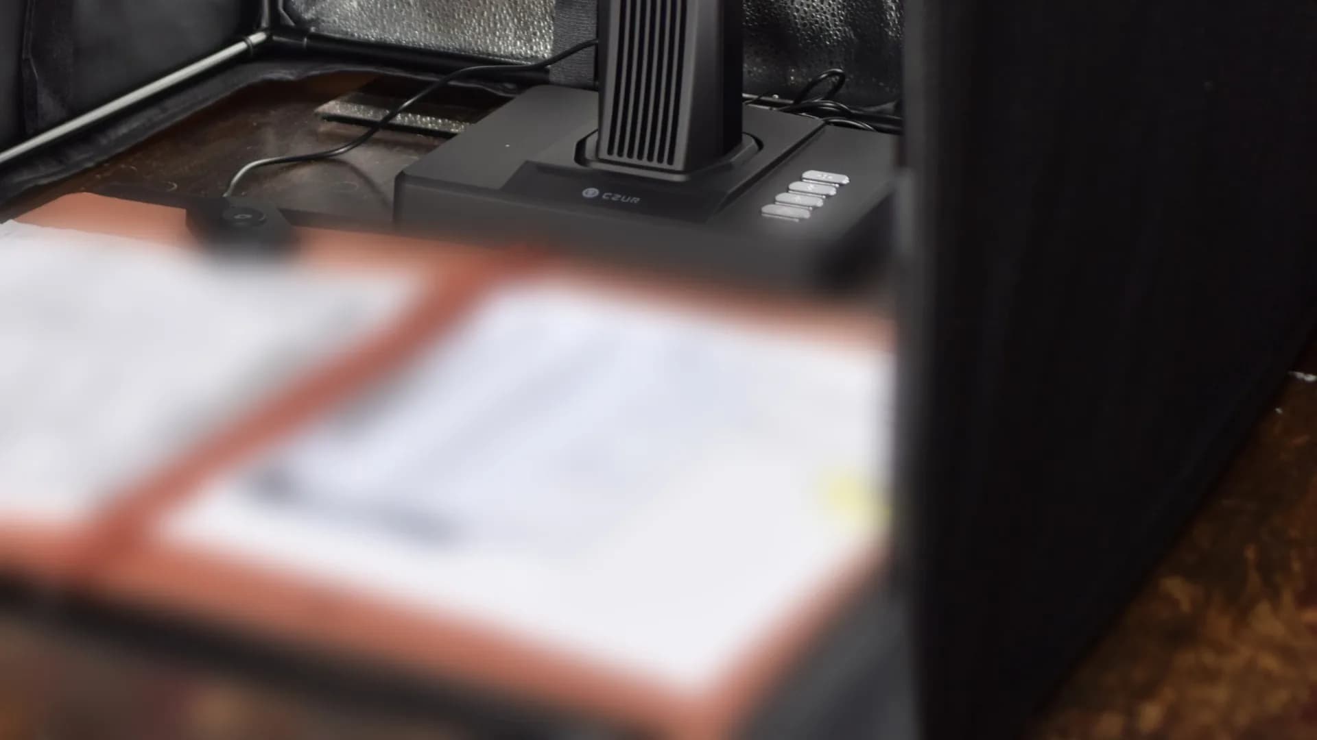 Escáner cenital CZUR de TUDIGI dentro de una cabina de luz, con carpetas de documentos